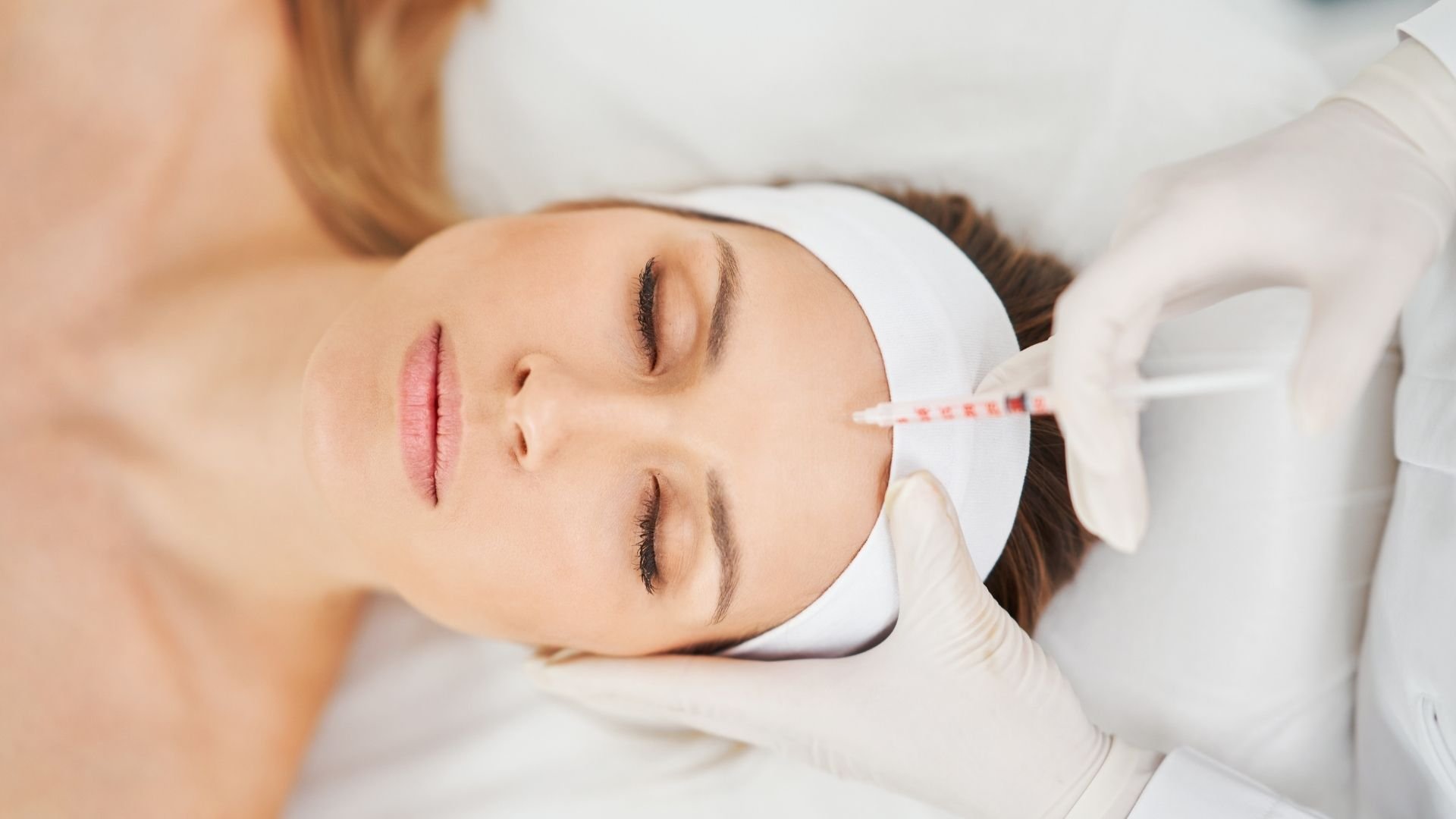 Woman receiving facial injection treatment from professional cosmetologist wearing white gloves