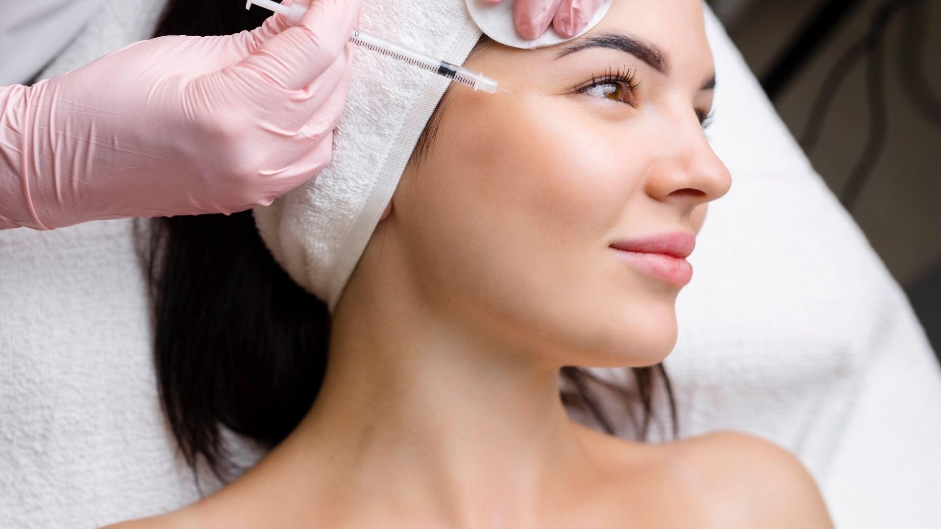 Aesthetician administering botox injection to woman's forehead with syringe