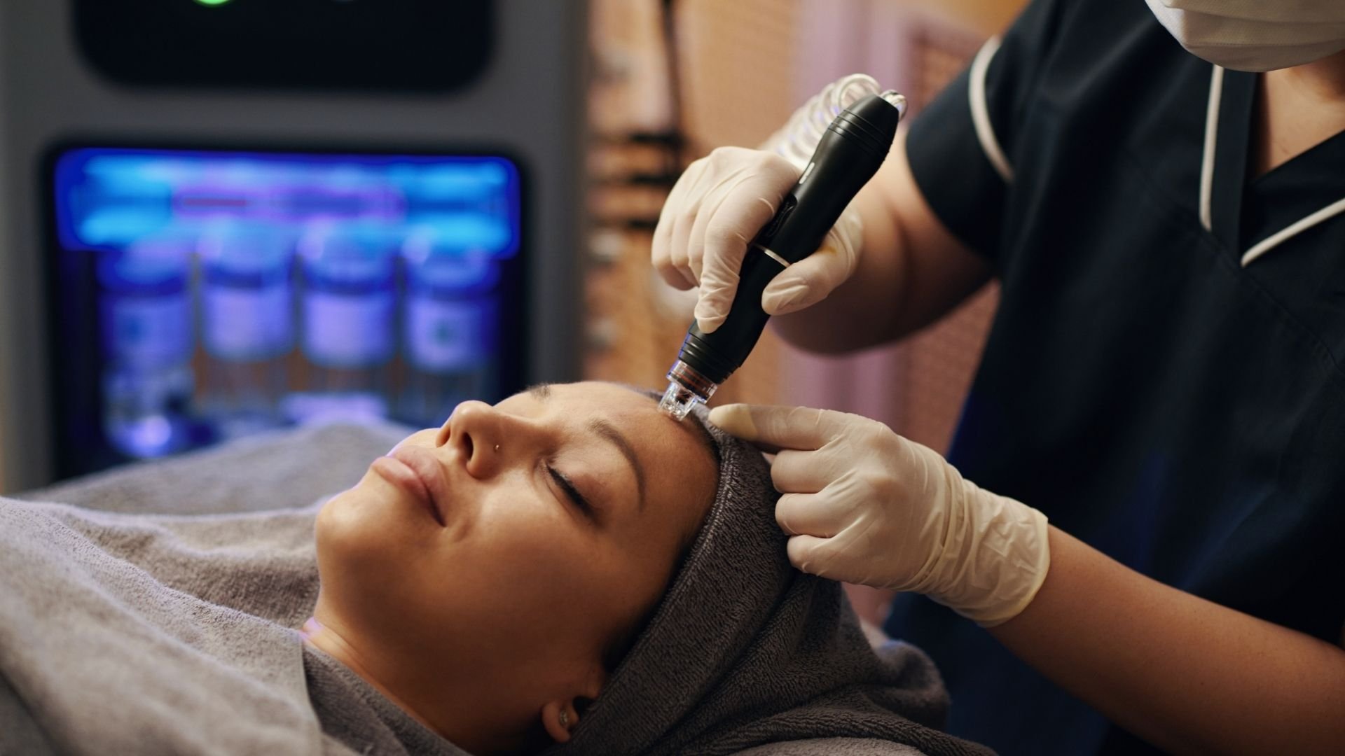 Esthetician performing microneedling treatment on client's face with handheld device.
