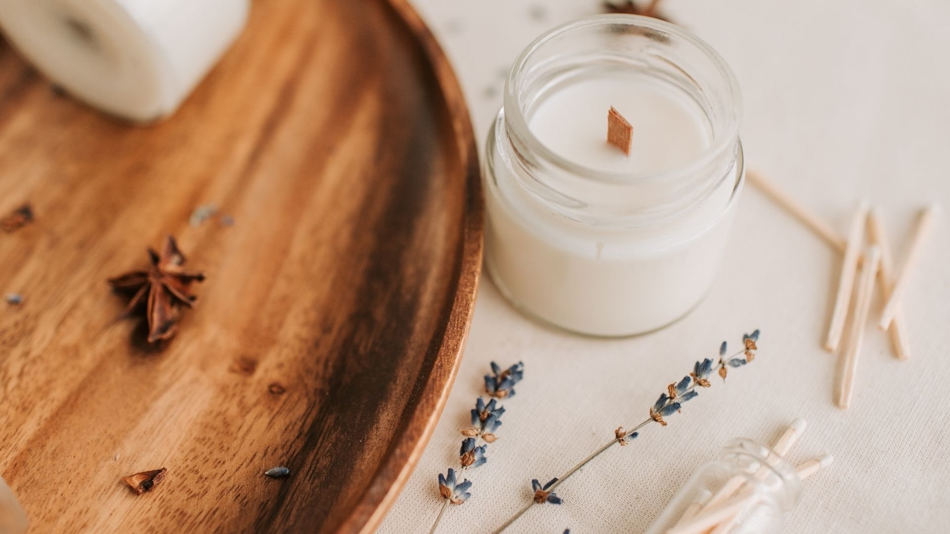 Wooden tray with star anise and wooden bowl beside lit scented candle with lavender sprigs